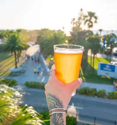 A hand holding a cold pint of craft beer from the balcony of 3 Daughters Brewing in Clearwater Beach on a sunny afternoon.