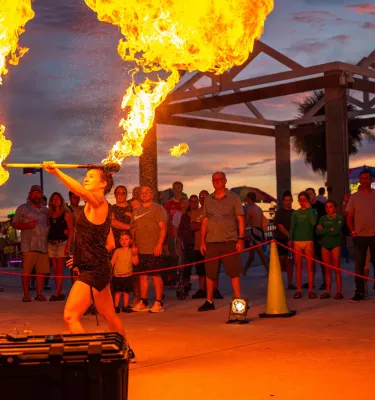 a woman in black shorts and tank top juggles with fire while spectators watch at Pier 60 in Clearwater Beach