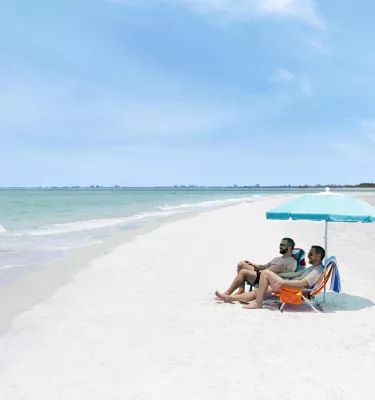 Couple sits under an umbrella on a wide, white-sand beach