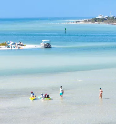 People wade in clear water with two islands nearby.