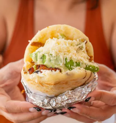 a woman in a tank top holds a large arepa in her hands