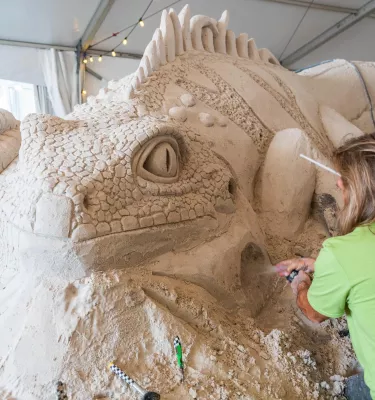 an artist in a lime green shirt creates a dramatic and detailed iguana sand sculpture