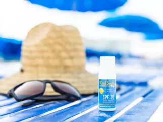 Una toalla de playa con un sombrero de paja, gafas de sol oscuras y una pequeña botella de protector solar seguro para los arrecifes.