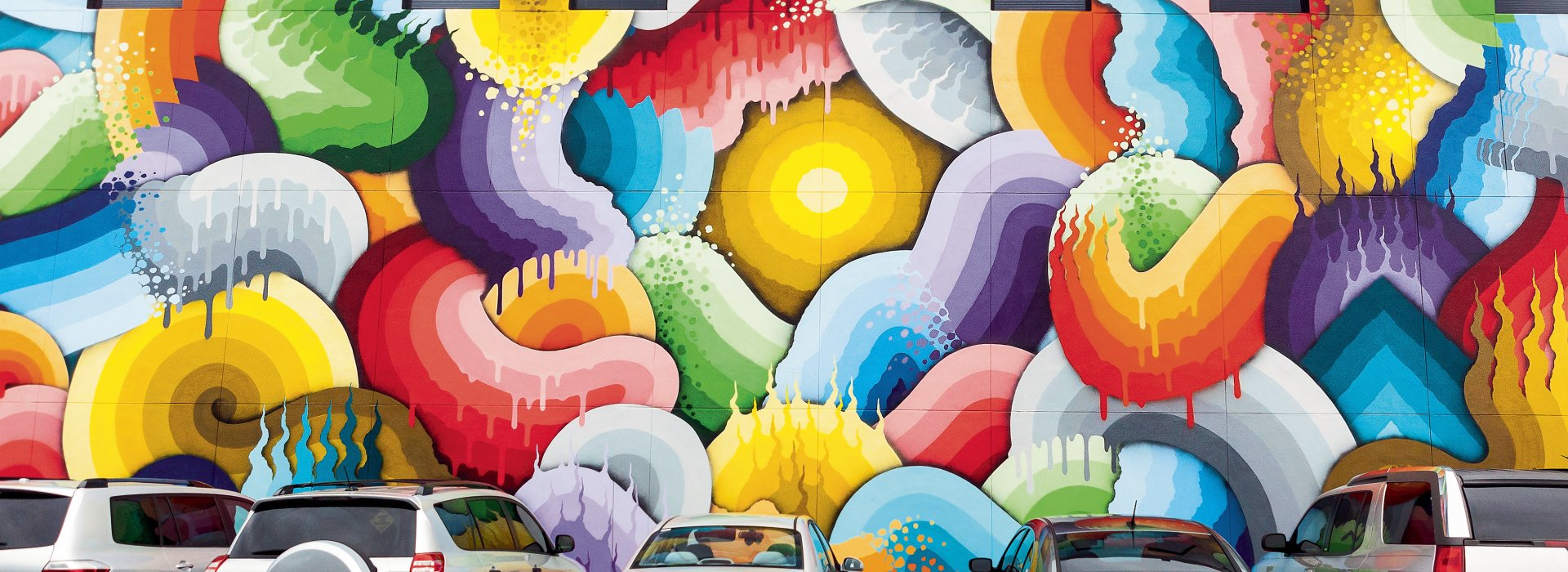 Several cars parked in front of a colorful mural