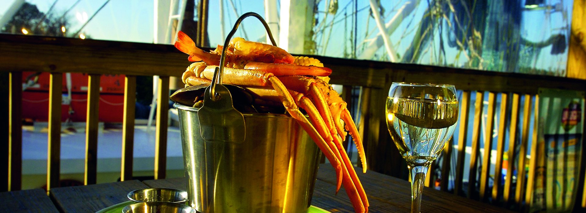 A bucket of crab legs and a glass of white wine over an outdoor table from the Rusty Bellies Restaurant