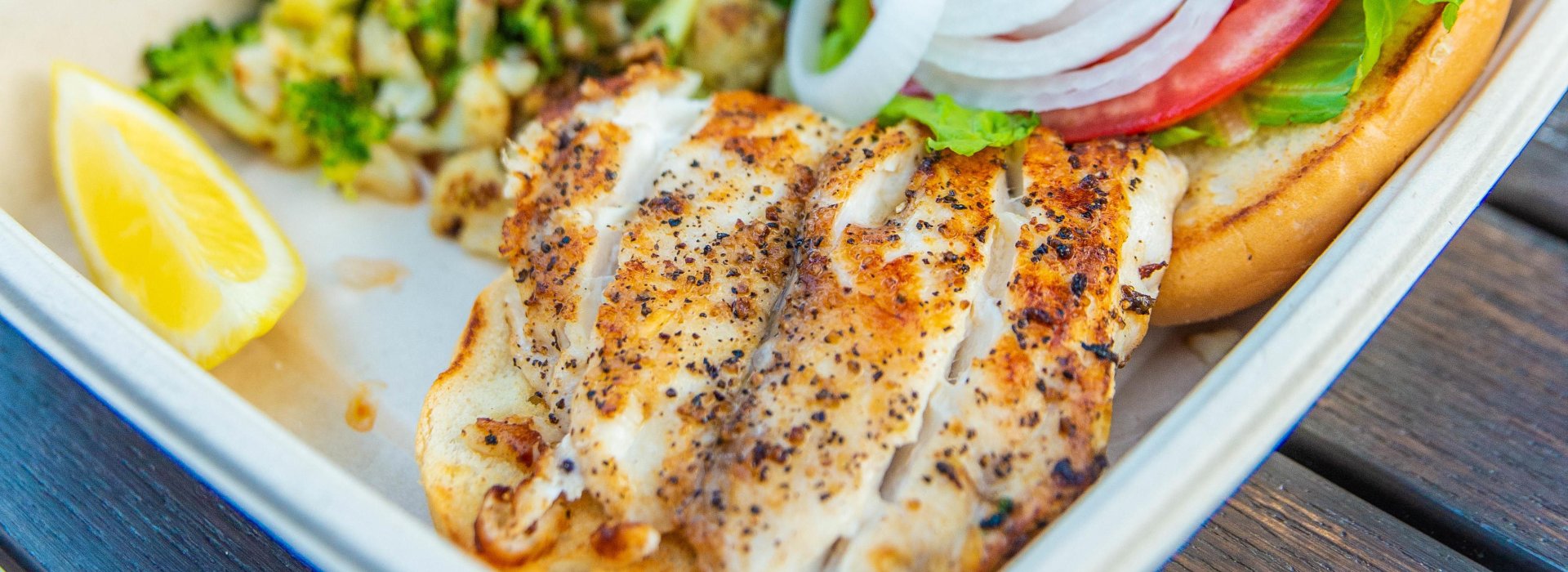 A close view of a grouper fish plate with onions, tomatoes and green vegetables.