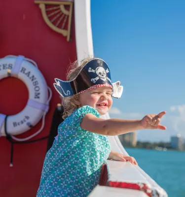 A happy little girl wearing a pirate hat on board Captain Memo's Pirate Cruise.
