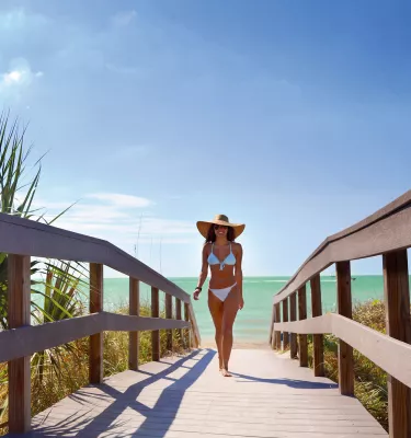 A young lady dressed in bikini walking Indian Rocks Beach boardwalk.