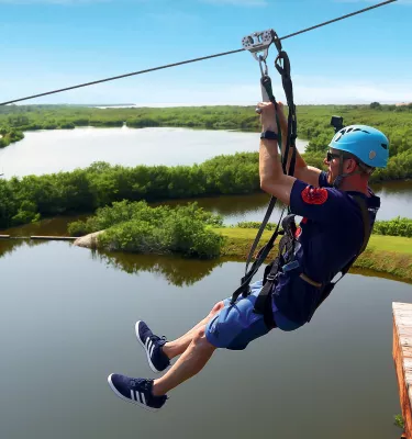 a man ziplines above Mobbly Bayou Wilderness Preserve in Oldsmar; a lake and trees can be seen below him