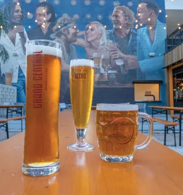 Three glasses of beer on top of an outside table in front of a large mural at the Grand Central Brewery in St. Pete.