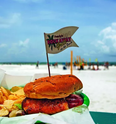 A grouper sandwich with fries at an outdoor patio with a view to the beach. Beach goers can be seen at a distance.
