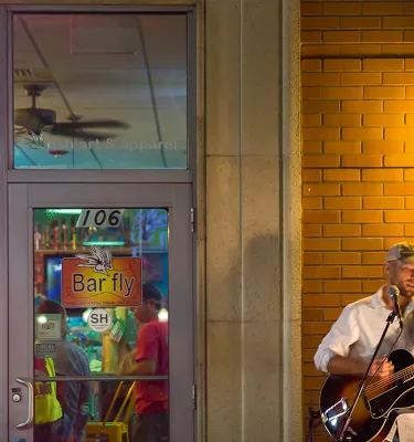 A musician playing guitar and singing outside of the Bar Fly in Safety Harbor at night.