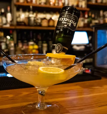 A yellow cocktail with lime and bottle of prosecco at the bar at Gigglewaters Bar