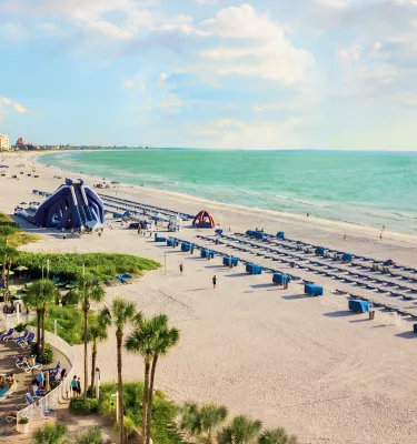 Übersicht über den Strandpool des Tradewinds Resorts mit blauen Cabanas, einer Wasserrutsche und aquamarinblauem Wasser.
