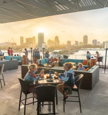 Several people enjoying drinks and meals while watching the sunset and St. Pete skyline from the rooftop of Pier Teaki.