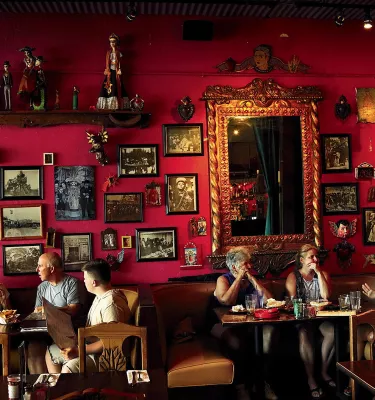 Six dinners eating at Casa Tina restaurant in Dunedin. The wall is red and decorated with multiple portraits.