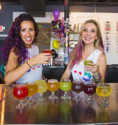 Two servers hold up a beer in front of more beer at Hawthorne Bottle Shop
