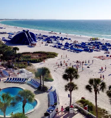Arial view of Tradewinds Hotel Showing the pool by the beach, beach chairs lined on the beach and there iconic giant blowup slide.