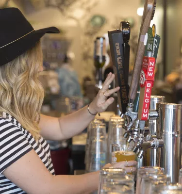 A lady wearing a black hat pouring beer from the draft.