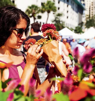 A young lady wearing sunglasses smelling flowers on display.