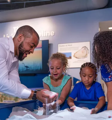 A Black family playing with sand at the Tampa Bay Watch Discovery Center at the St. Pete Pier