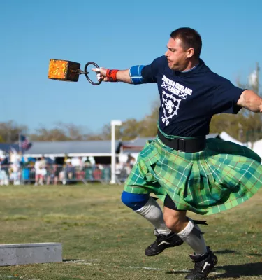 A man in a green kilt throws a weight competitively.