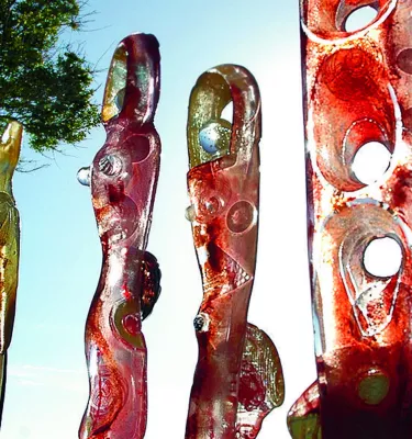 Five sculptures in a line next to a palm tree with the sunlight in the background.