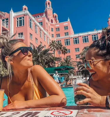 Two ladies with colorful drinks laughing at the pool of Don CeSar hotel