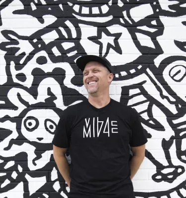 An artist stands in front of a large mural he painted