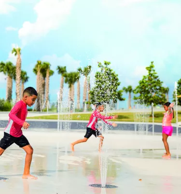 Three children play at the splash pad at St. Pete Pier with palm trees in the background