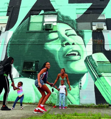 Children and parents playing outside in front of a wall mural in the Deuces Live district during the day.