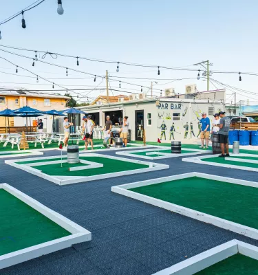 Outside image of mini-golf bar Par Bar, featuring various holes, string lights and giant beer pong.