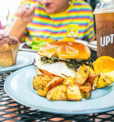 Food plates of an egg and spinach sandwich with roasted potatoes and a pastry.