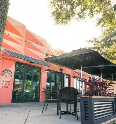 Exterior shot of Wild Child restaurant featuring decorated pink walls, black outside seating and trees.