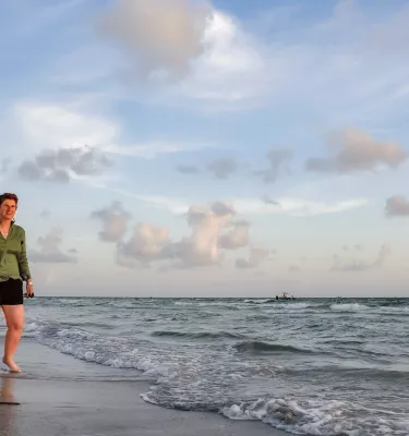two women hold hands while walking at the water's edge at the beach