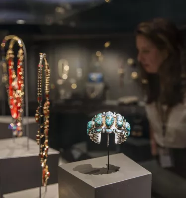 a woman looks at a glass case of Native American jewelry including a turquoise bracelet at the James Museum