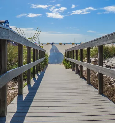 boardwalk to beach lined with dunes, with a large inflatable water slide on the left, the sky is blue with puffy white clouds