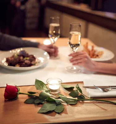 Couple having dinner with a single rose on the table, white plates with food, and a champagne toast.
