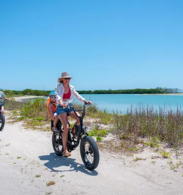 Family on ebikes rides along a sandy path by the water