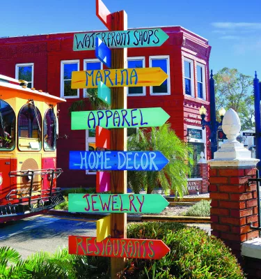 A colorful direction sign is in front of a trolley and shops.