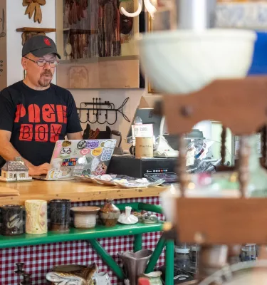 Man behind store counter surrounded by eclectic crafts.