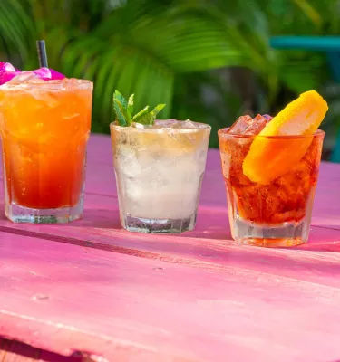 5 tropische Cocktails, garniert mit Früchten auf einem rosa Tisch im Freien