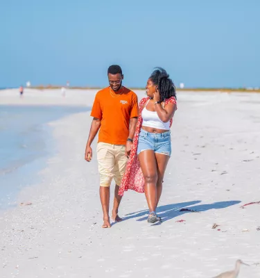a young couple in casual clothes walking on a white sand beach