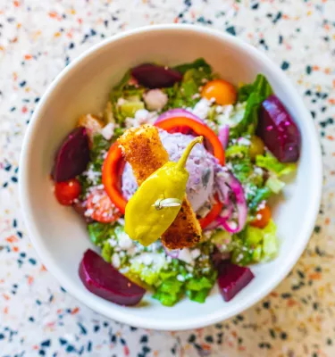 a colorful bowl of greek salad with beets and a pepperocini