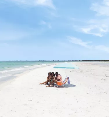 a mom, dad and little girl sit under a beach umbrella at Fort De Soto Park's beautiful white-sand beach