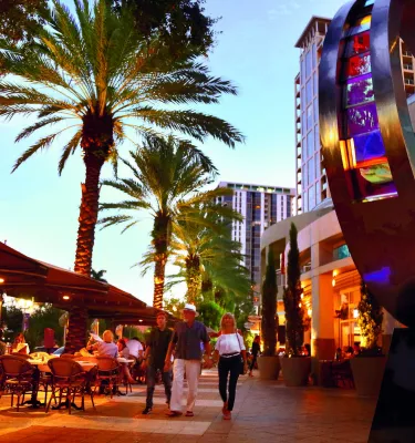 dusk image of people walking on Beach Drive and cafe diners, with a circular sculpture on the right side