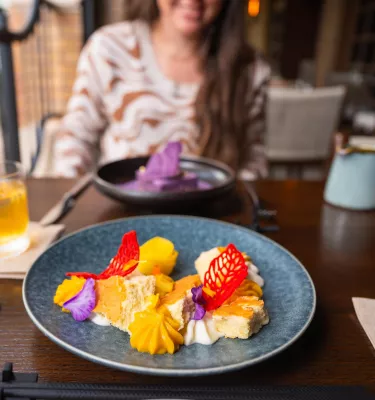 a colorful plate of food with cocktail surrounding it and a young woman in the background at Fortu restaurant