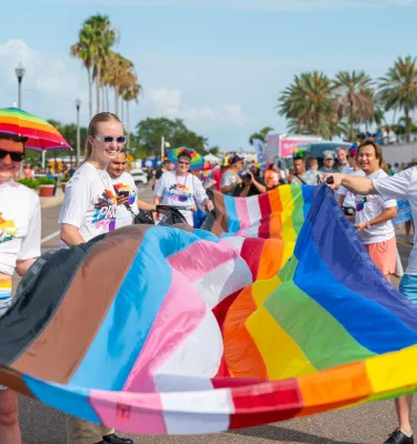 people in rainbow colored clothing carrying a pride flag in a parade