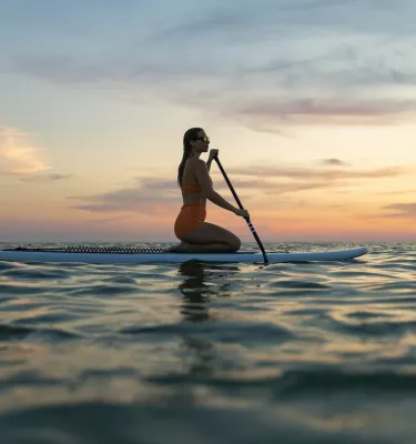 a woman kneeling on a paddleboard at sunset