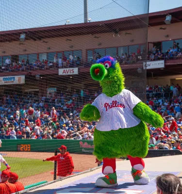 the Philadelphia Phillies mascot is shown with baseball players on the field and a full crowd in the stands